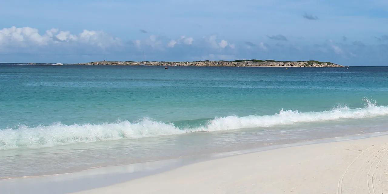 Vague sur sable blanc de la Baie Orientale avec Caye Verte en arrière-plan