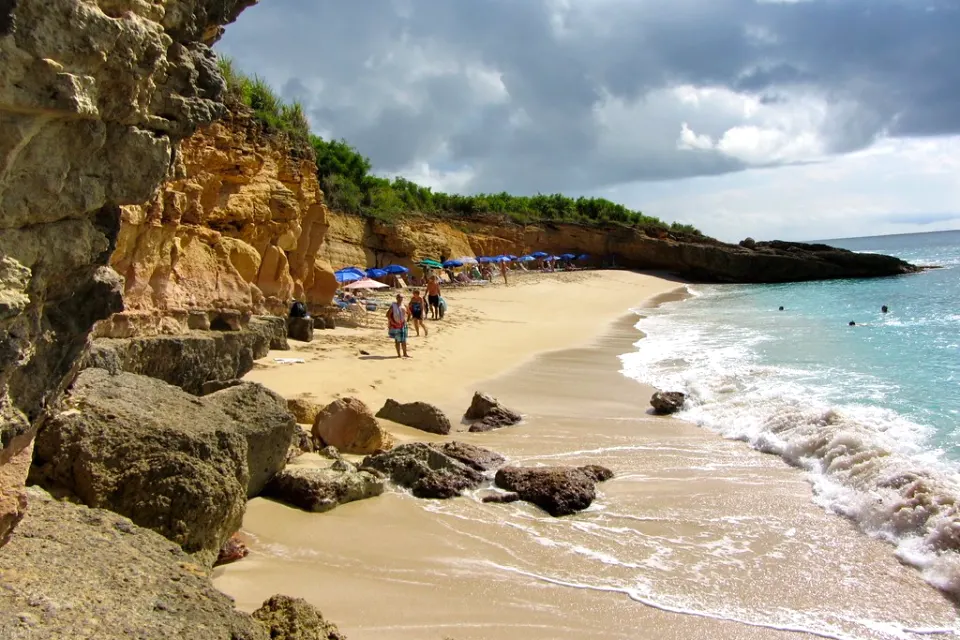 Plage de Cupecoy au pied des falaises ocre avec transats et vagues sur le rivage