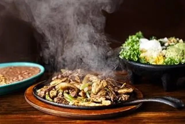 Fajitas de boeuf grésillantes servies sur plaque en fonte fumante chez 3 Amigos