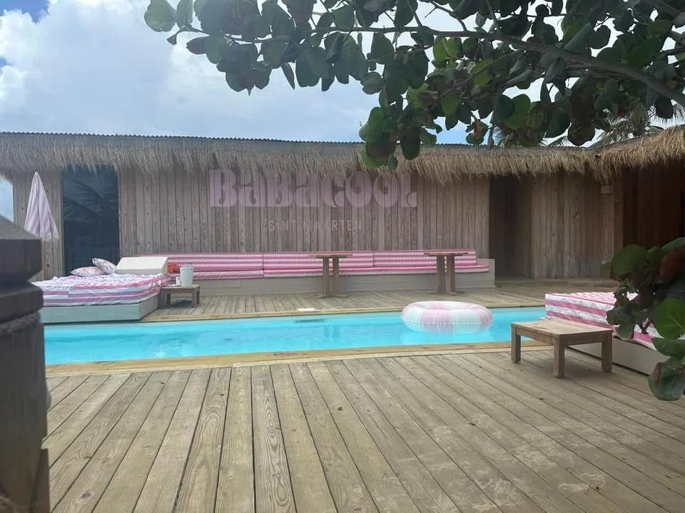 Piscine de Babacool avec daybeds rayés rose et fronton en bois marqué BABACOOL Sint Maarten
