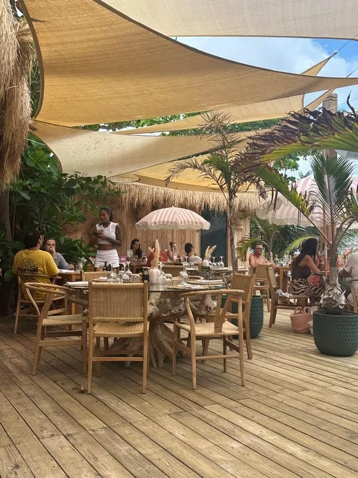 Tables du restaurant Babacool sous voile d'ombrage et palmiers, déjeuner les pieds dans le sable