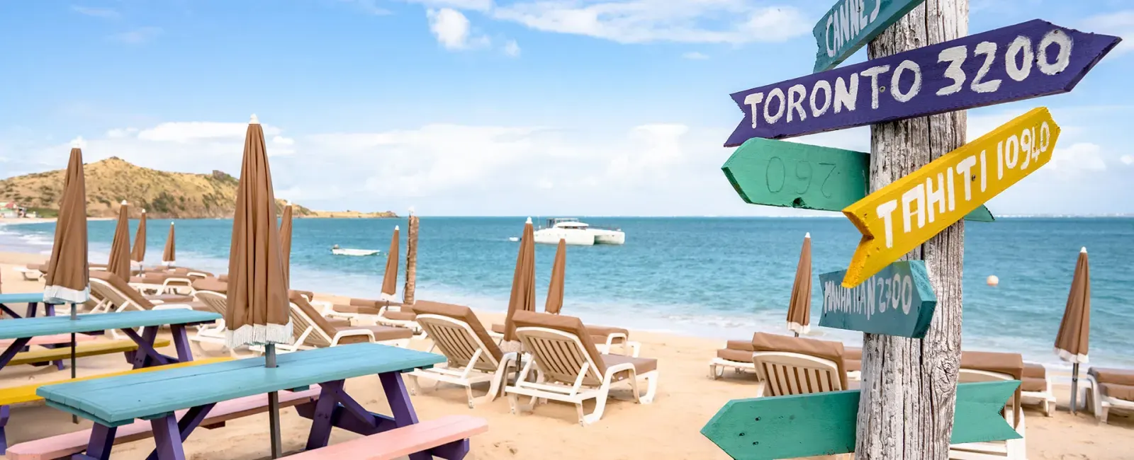 Captain Frenchy - tables de pique-nique colorées et panneau Tahiti Toronto sur la plage de Grand Case