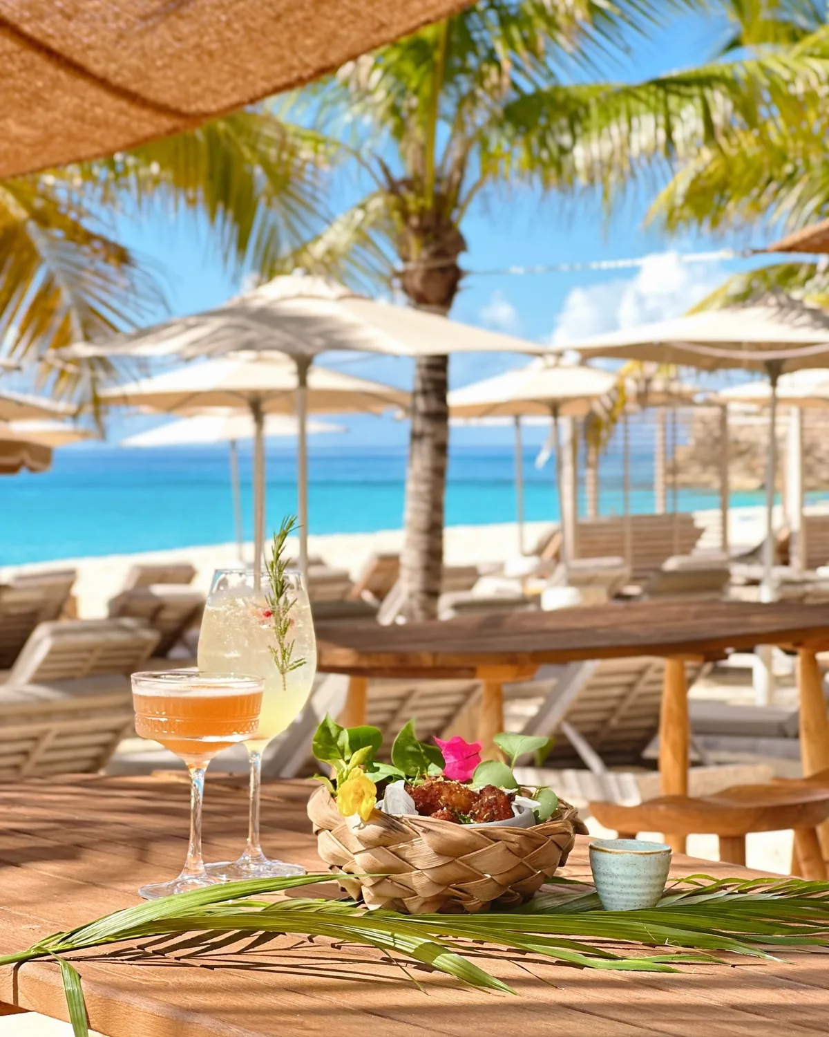 Cocktails et mezzé sur table en bois face à la plage de Kalatua, ambiance Tulum
