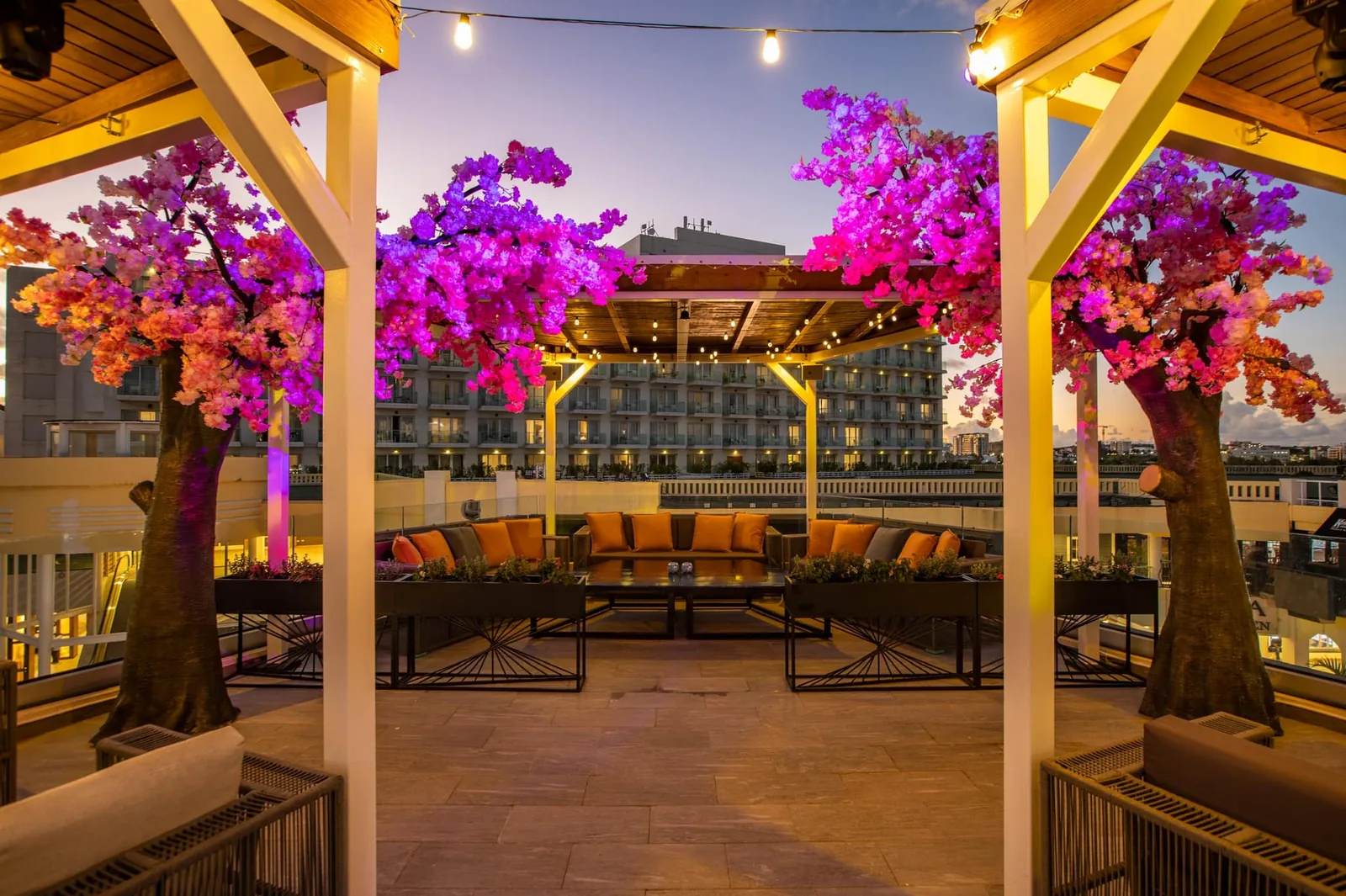Toit-terrasse de Mimosa Skylounge à Maho au crépuscule avec arbres en bougainvilliers roses et banquettes orange