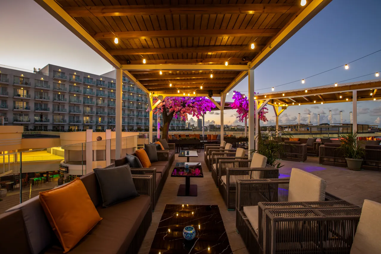 Tablée et sofas du rooftop Mimosa Skylounge sous les bougainvilliers illuminés