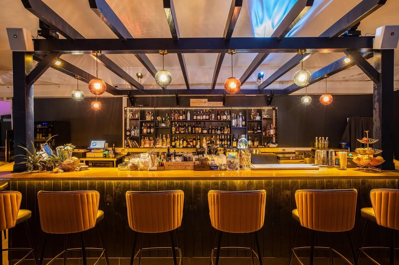 Bar de Mimosa Skylounge avec tabourets en velours moutarde et lustres en verre