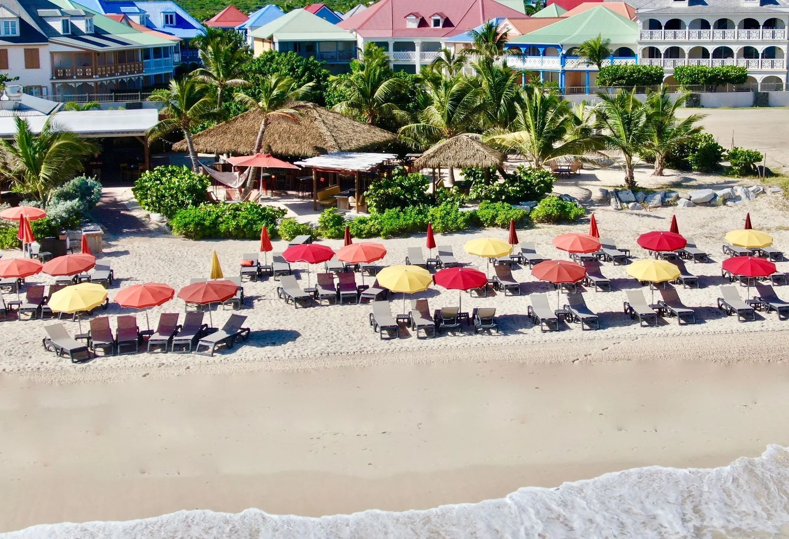 Vue aérienne de Waï Plage à la Baie Orientale avec parasols rouges et jaunes alignés sur le sable blanc