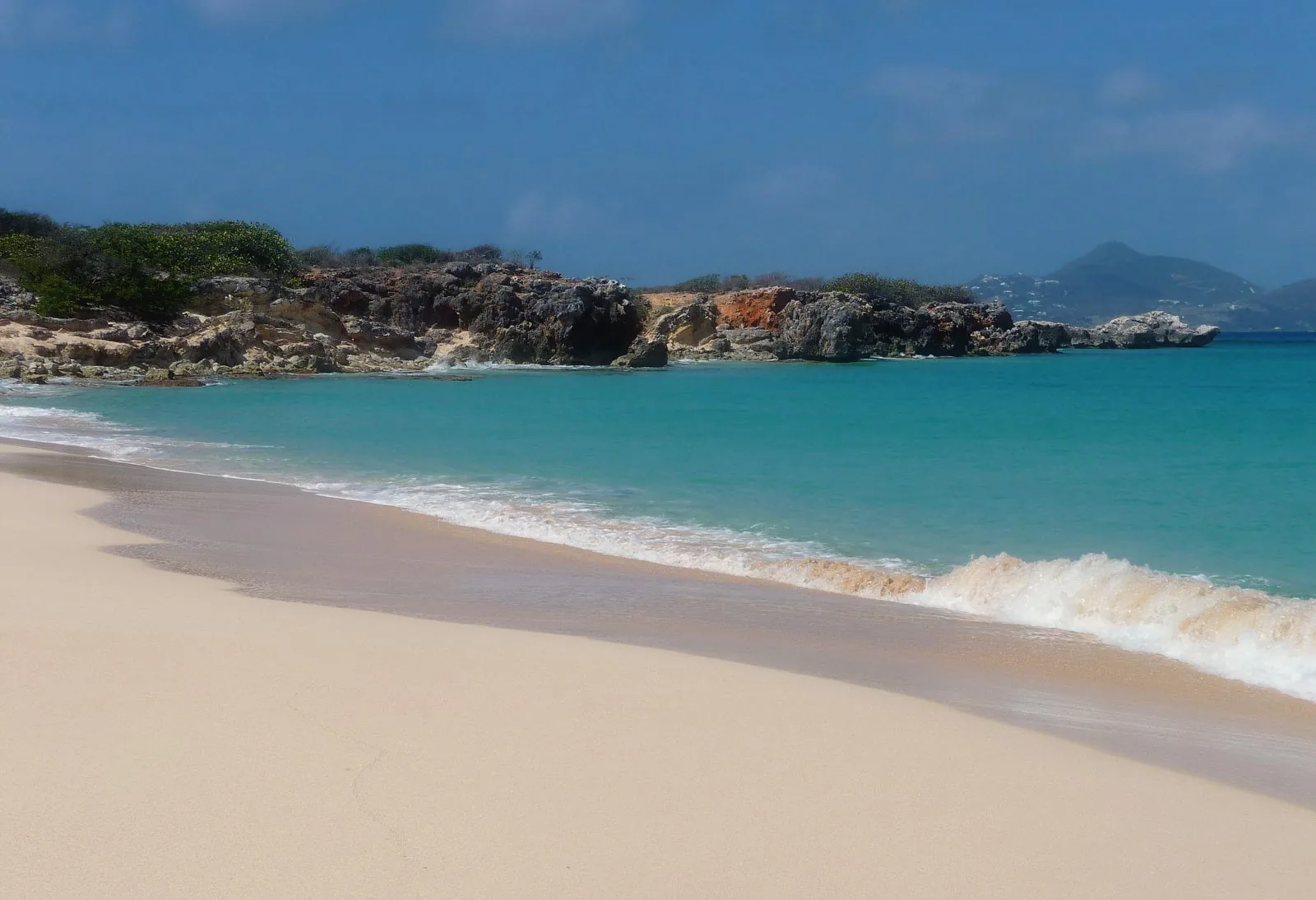 Plage déserte de Baie Blanche à Tintamarre avec sable blanc, eau turquoise et rochers, vue vers Saint-Martin